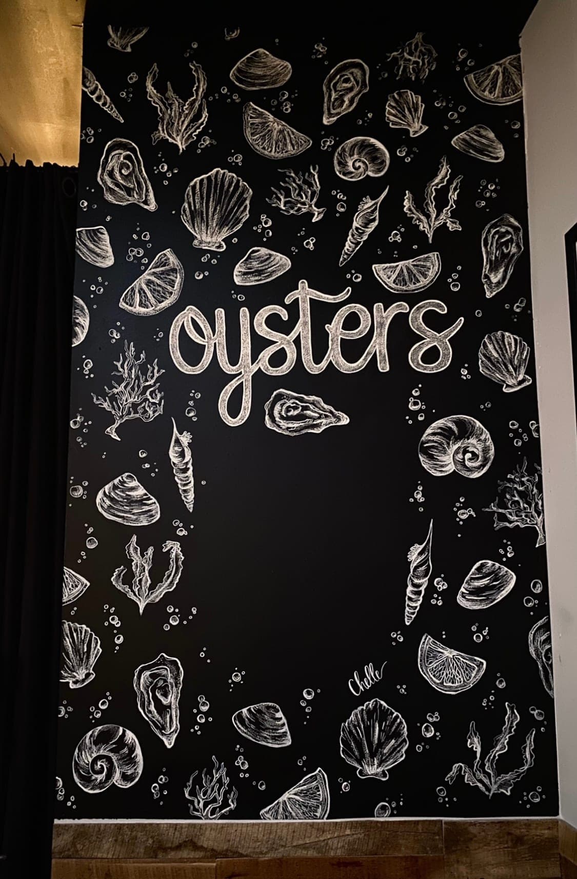 Tall black wall lettered "Oysters" in white and framed by drawn shells, seaweed and lemon slices