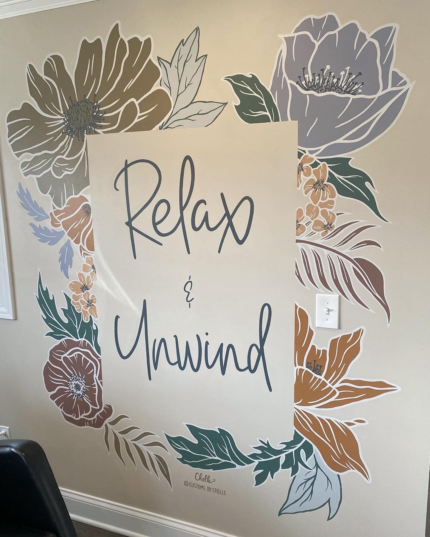 "Relax & Unwind" painted in script inside a border of muted flowers and leaves on the same salon wall